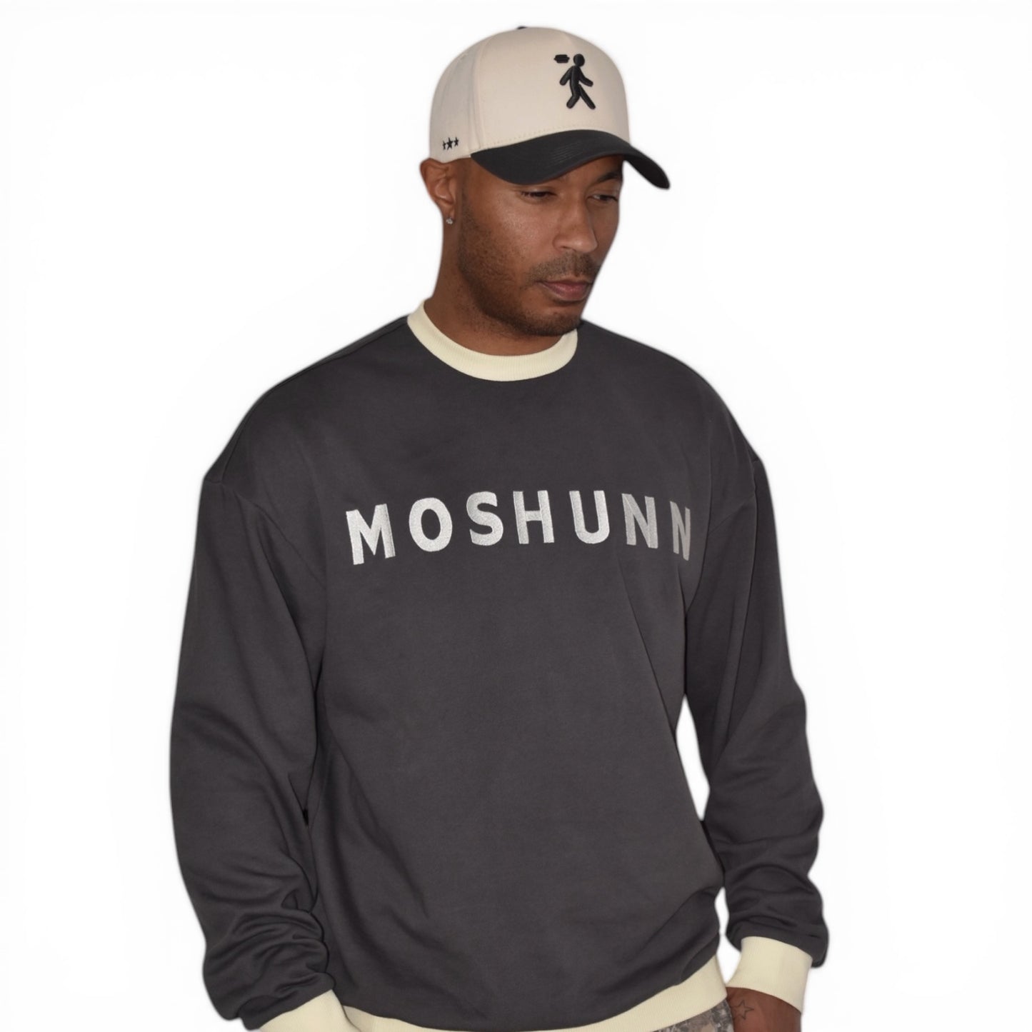 Man wearing a charcoal gray crewneck with 'MOSHUNN' text and a cap on a white background