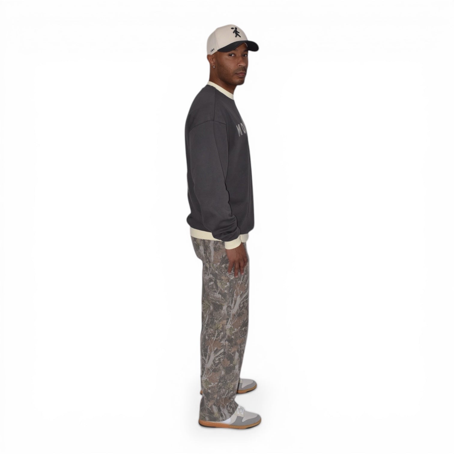 Man wearing a charcoal gray crewneck light pants, and a cap on a white background