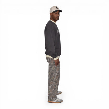 Man wearing a charcoal gray crewneck light pants, and a cap on a white background